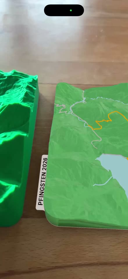 A single-color printed terrain model on a table, beside the same model shown in color as an augmented-reality preview on an iPhone.